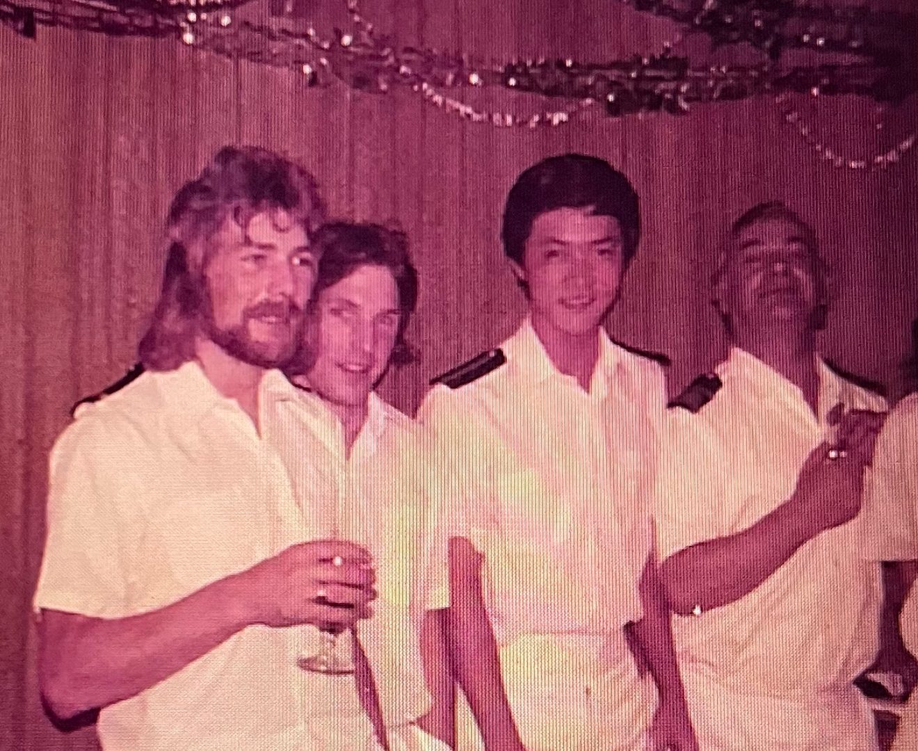 Vintage photo of four men in white uniform shirts with epaulets at a party, reddish tint.