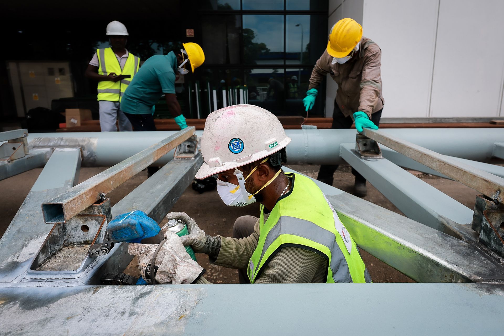 A worker (foreground) conducting a magnetic particle inspection on welded steel gantry components.