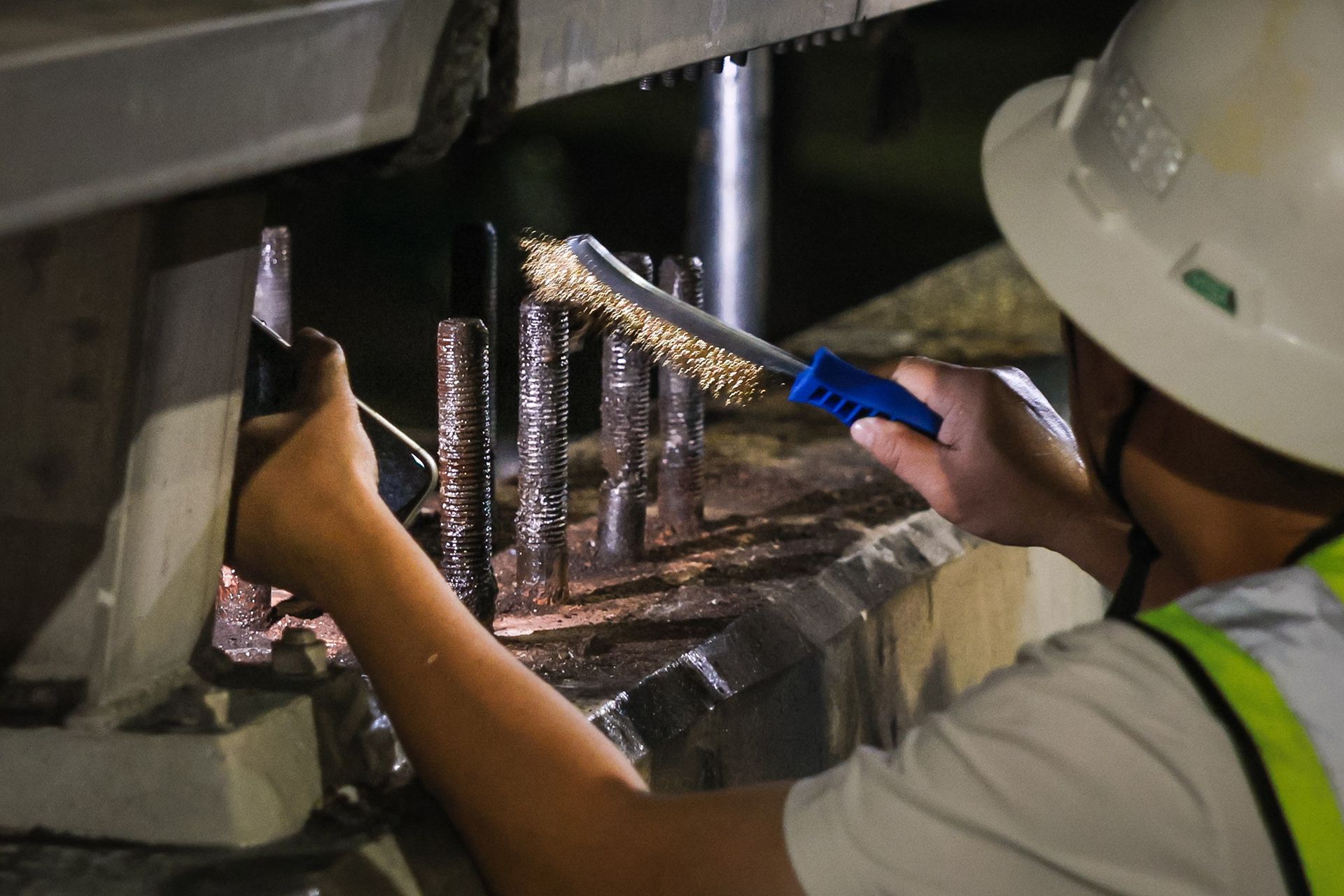 A worker cleaning the bolts and fasteners after removing the existing overhead road gantry.