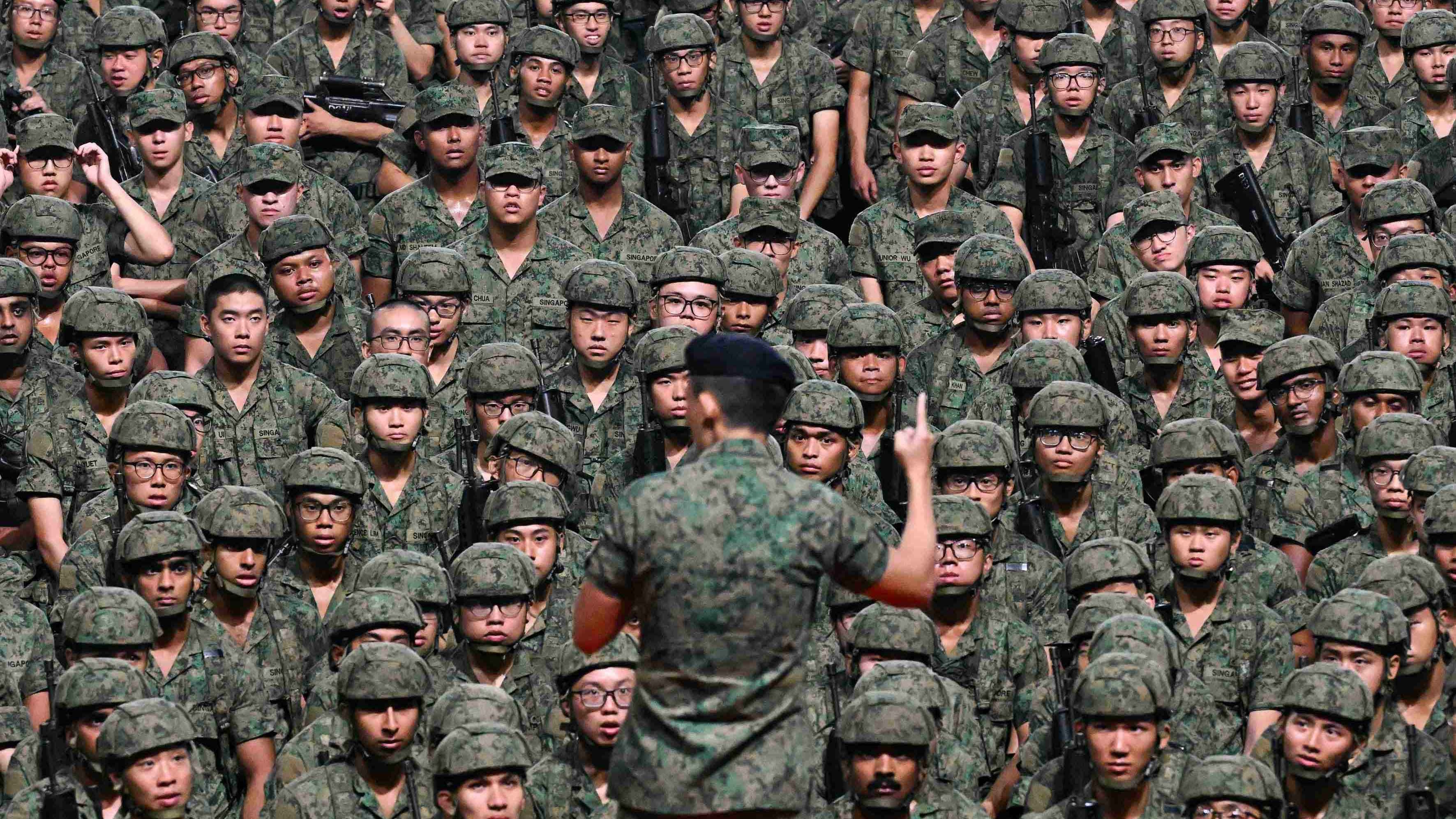 Group of people in singapore army uniform sitting in rows receiving instructions from a superior
